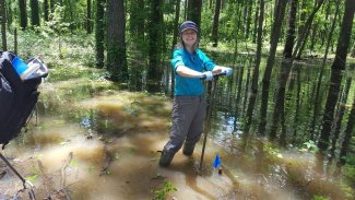 Field technician soil sampling in a forest floodplain at the DELA field site